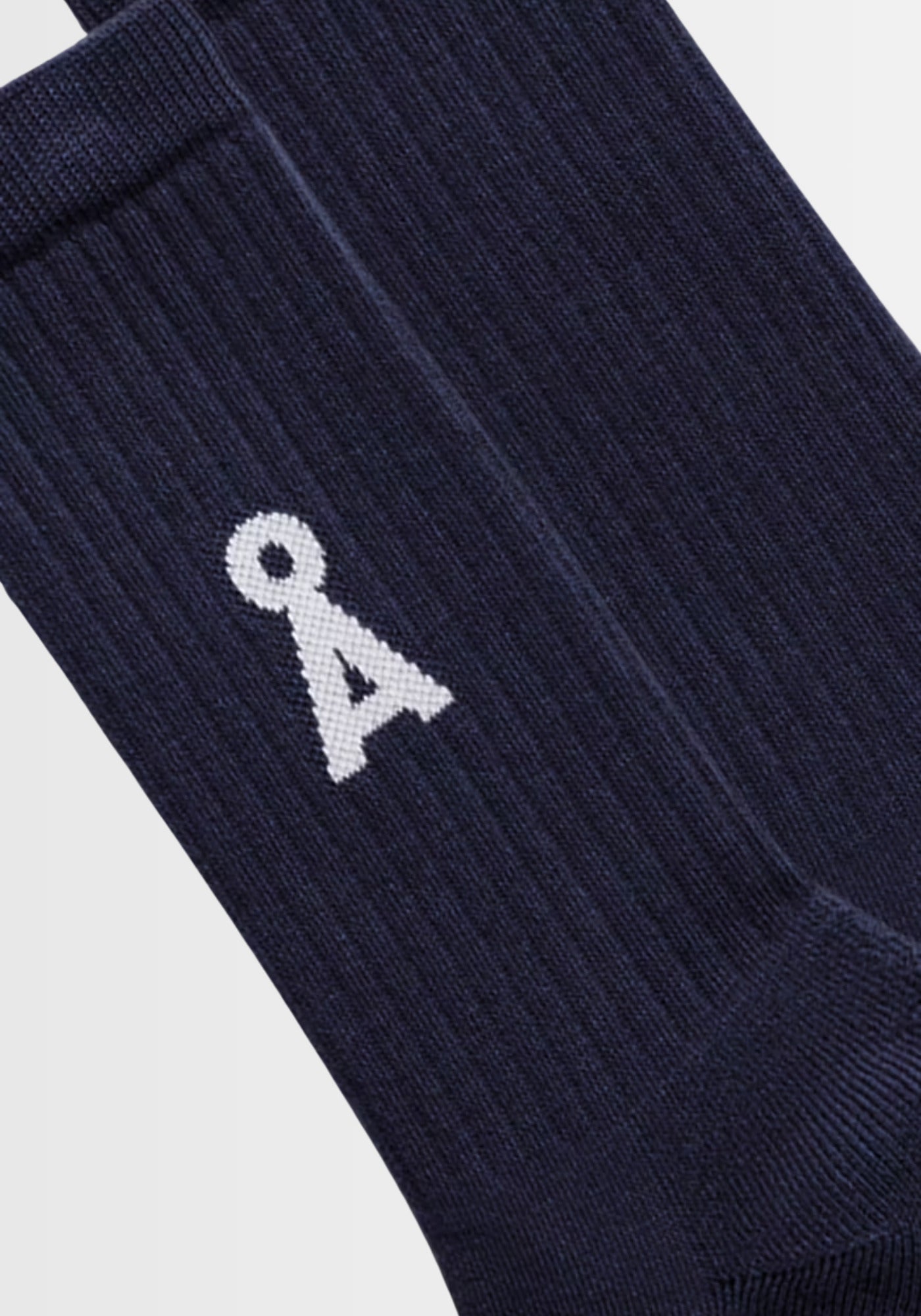 Das Modell präsentiert die schwarzen SAAMUS BOLD Socken in „night sky“ mit auffälligem A‑Logo, gefertigt aus 78% Bio‑Baumwolle, 20% recyceltem Polyamid und 2% Elasthan für optimalen Komfort.
