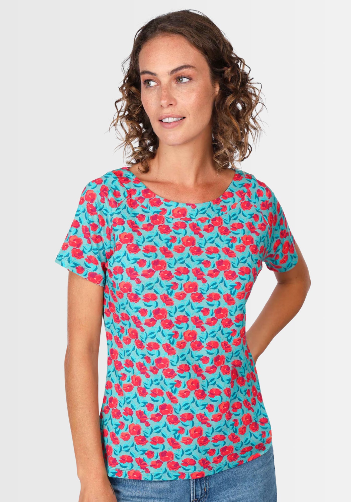 Lifestyle-Aufnahme des T-Shirts „Zoe rosy“ in Türkis. Getragen mit einer hellen Jeans und Sandalen, unterstreicht das floral bedruckte Oberteil aus nachhaltiger Viskose den femininen, sommerlichen Stil.