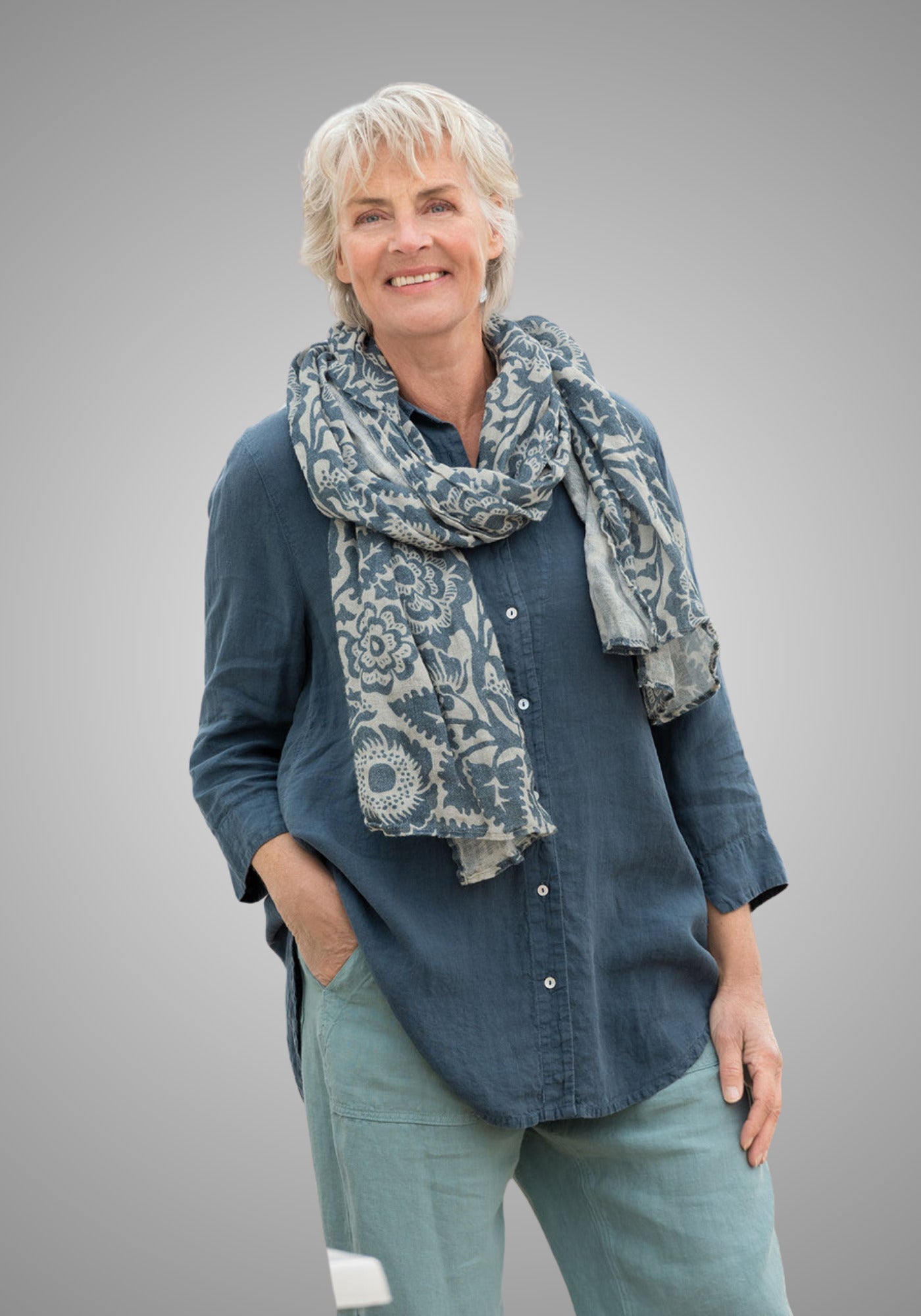 Frau trägt den dunkelblauen Leinenschal Tinna mit floralem Print in Dark Denim, kombiniert mit einem lässigen Leinenhemd für einen entspannten Freizeitlook.