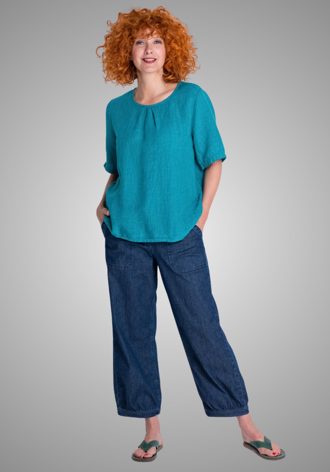 Model trägt das kurzärmelige Blusenshirt aus reinem Leinen in der Farbe Mangold, mit dekorativen Falten am Rundhalsausschnitt.

