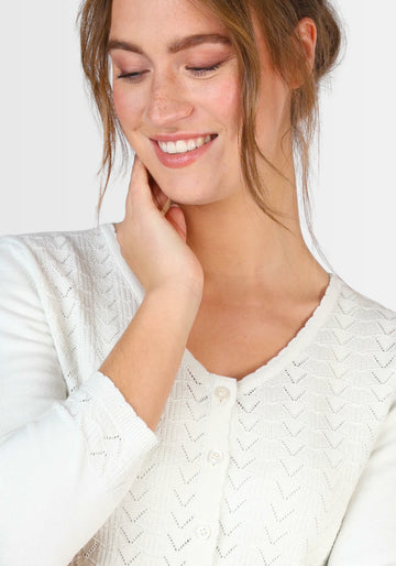 Nahaufnahme des feinen Ajourmusters und der eleganten Knopfleiste der Strickjacke „Liselotte“ in Weiß. Die hochwertige Verarbeitung aus 100% Bio-Baumwolle spiegelt erstklassige Qualität wider.

