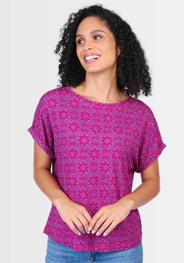 Lifestyle-Aufnahme des T-Shirts „Vroni“ in kräftigem Himbeerrot. Kombiniert mit Jeans und Sandalen entsteht ein femininer Boho-Look, perfekt für warme Tage und lockere Alltagsoutfits.

